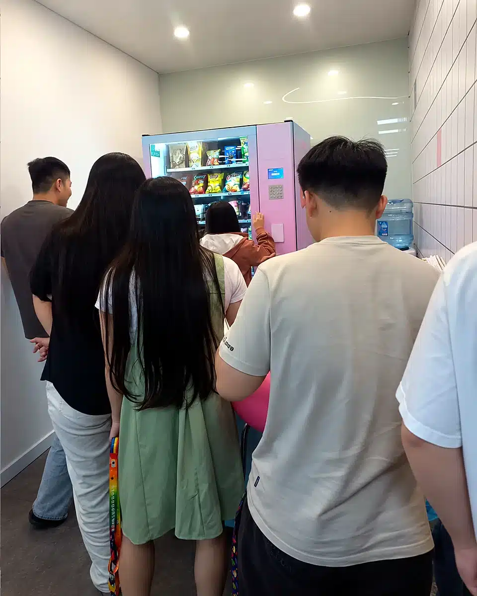 Nhân viên văn phòng xếp hàng mua đồ uống và đồ ăn nhẹ tại máy bán hàng tự động